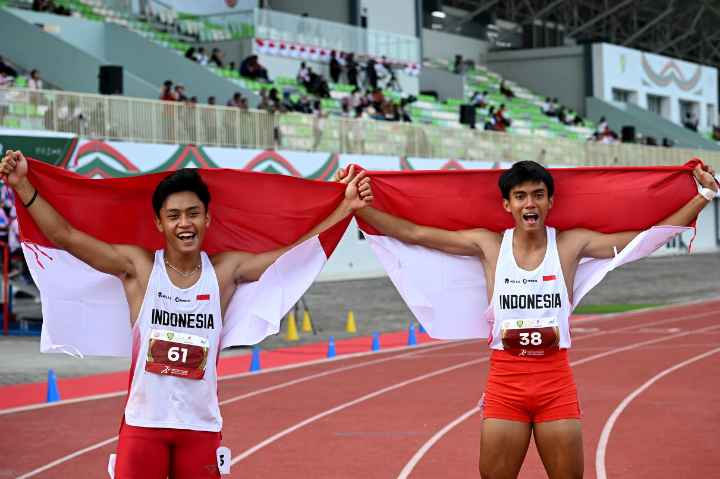 Atlet lari putra Indonesia Gilang Satria Wibawa (kanan) bersama Rizal Hafid Fuadi (kiri) melakukan selebrasi sambil memegang bendera merah putihn usai beradu kecepatan dengan atlet Thailand, Singapura, Malaysia dan Filipina pada nomor lari 200 meter U-18 dalam kejuaraan Atletik Asia Tenggara 2025 di Stadion Madya Atletik, Deliserdang, Sumatera Utara, Senin (17/11/2025).